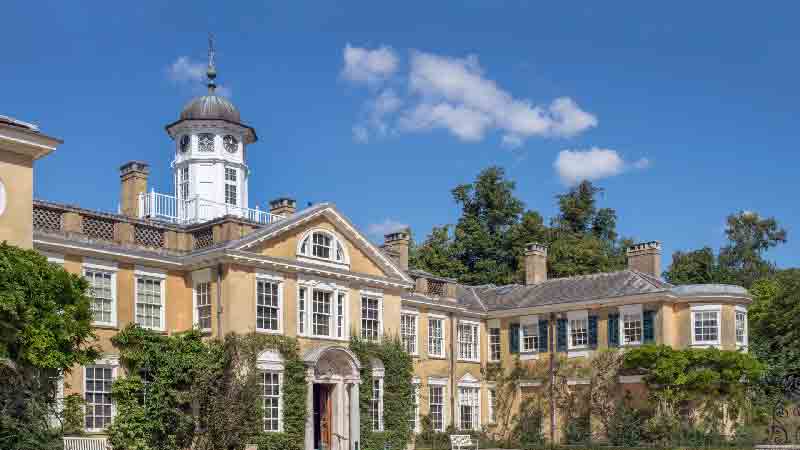 Polesden Lacey Manor in Surrey, a historic estate with elegant architecture surrounded by lush greenery and blue skies.