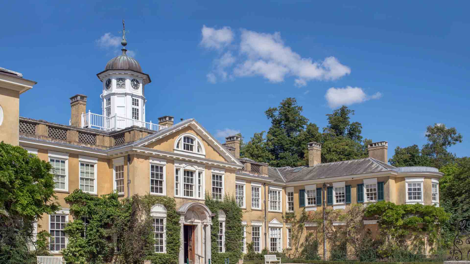 Polesden Lacey Manor in Surrey, a historic estate with elegant architecture surrounded by lush greenery and blue skies.