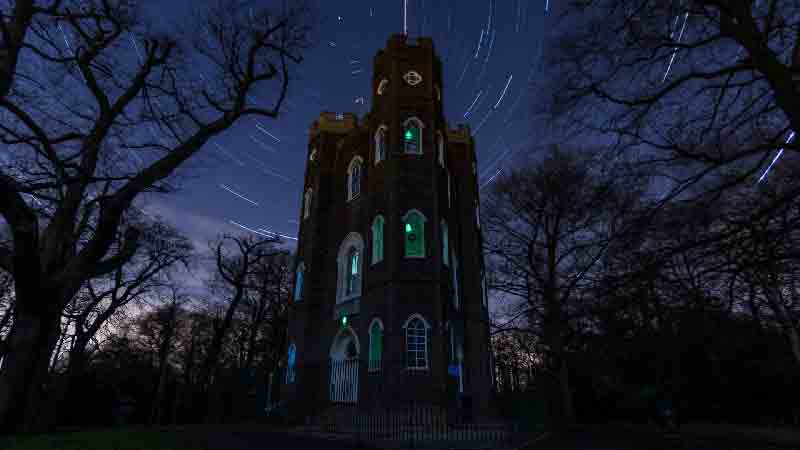 Severndroog Castle illuminated at night, with a star-filled sky and light trails.