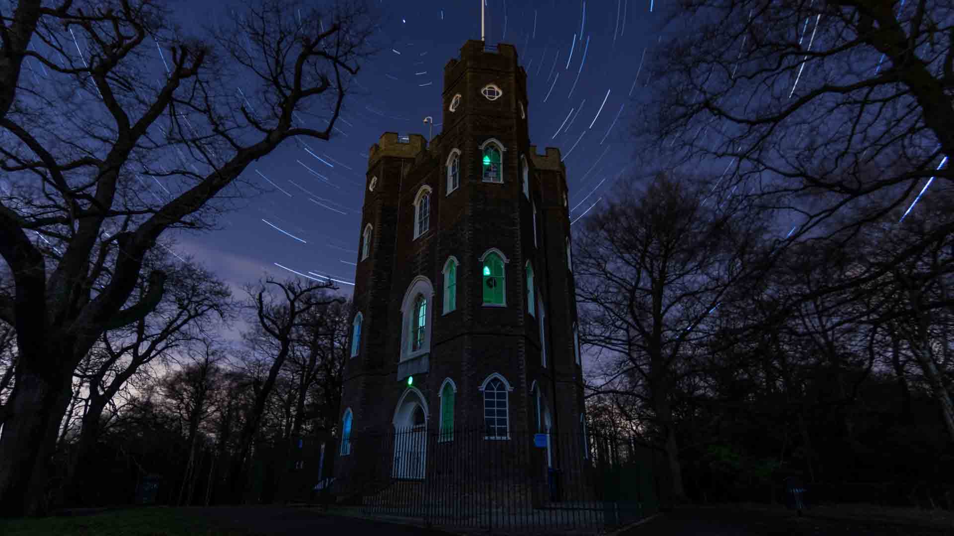 Severndroog Castle illuminated at night, with a star-filled sky and light trails.